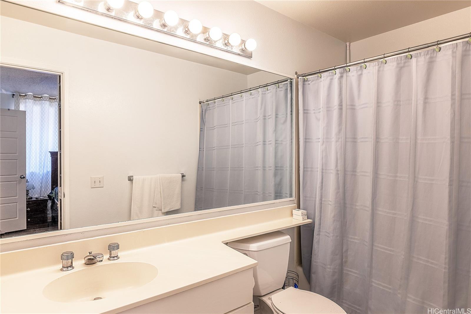91-957 Laaulu Street, Unit 40F Ewa Beach, HI 96706 - Photo 10 of 22 a bathroom with a sink a toilet a mirror and shower curtain
