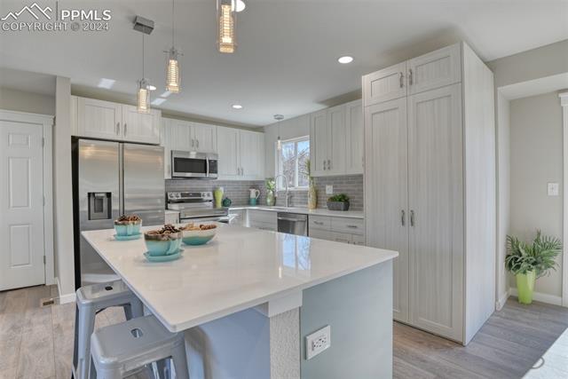 1913 Wooten Road Colorado Springs, CO 80915 - Photo 16 of 50 Kitchen with backsplash, stainless steel appliances, decorative light fixtures, and a kitchen bar