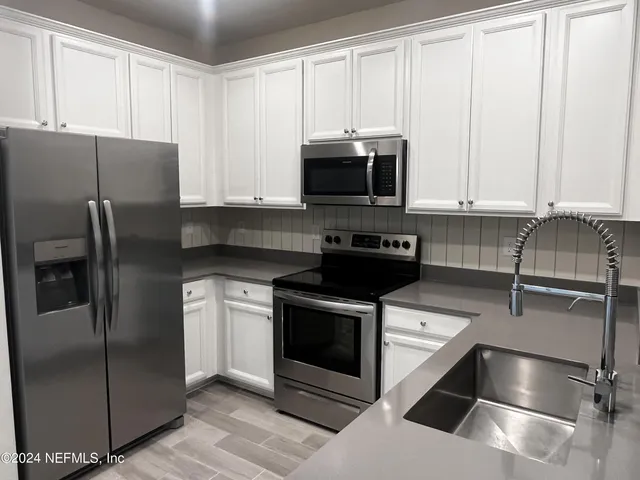 a kitchen with stainless steel appliances granite countertop a refrigerator a stove a sink and white cabinets