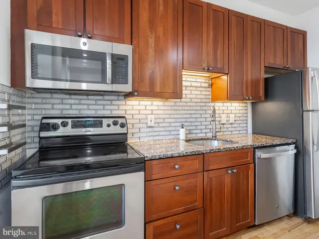 a kitchen with granite countertop wood cabinets stainless steel appliances and a sink