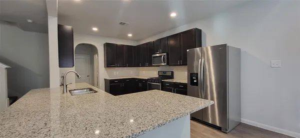 a kitchen with granite countertop a refrigerator a stove and a sink with wooden floor