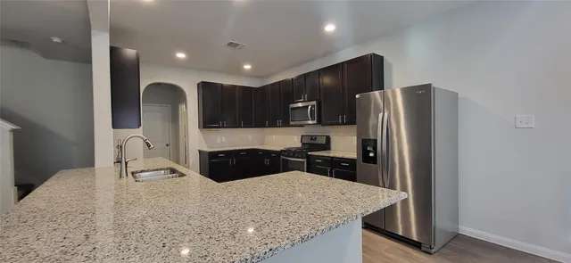 a kitchen with granite countertop a refrigerator a stove and a sink with wooden floor