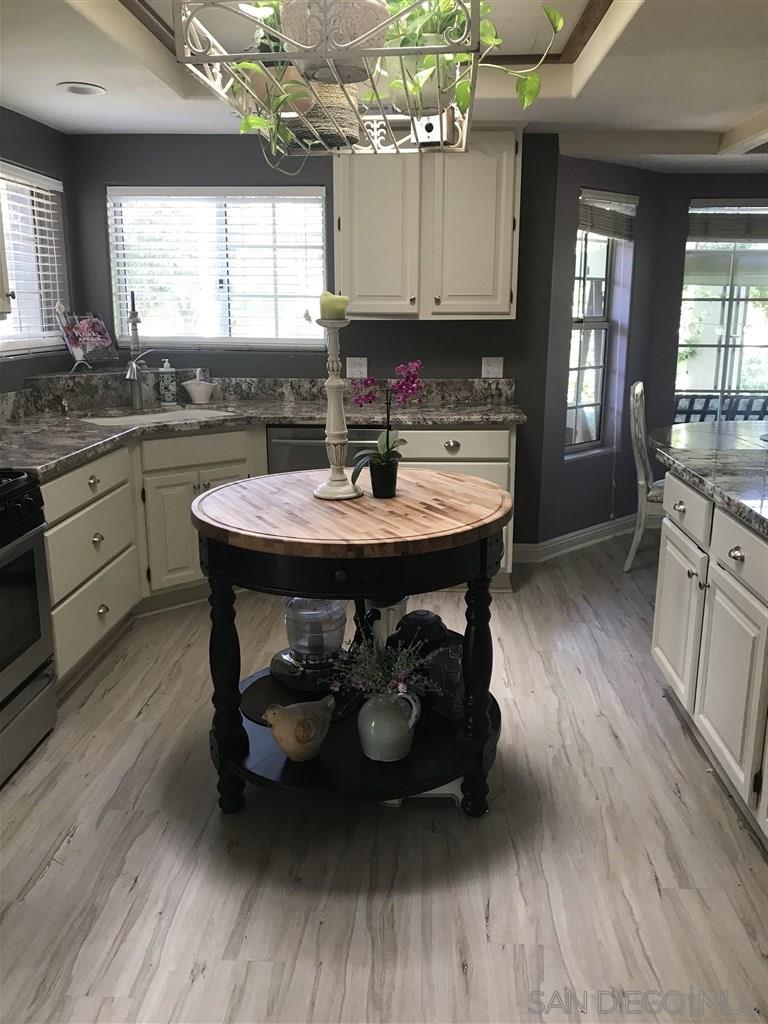 15950 Mactan Road Valley Center, CA 92082 - Photo 10 of 25 a kitchen with stainless steel appliances kitchen island granite countertop a sink dishwasher a stove a dining table and chairs with wooden floor