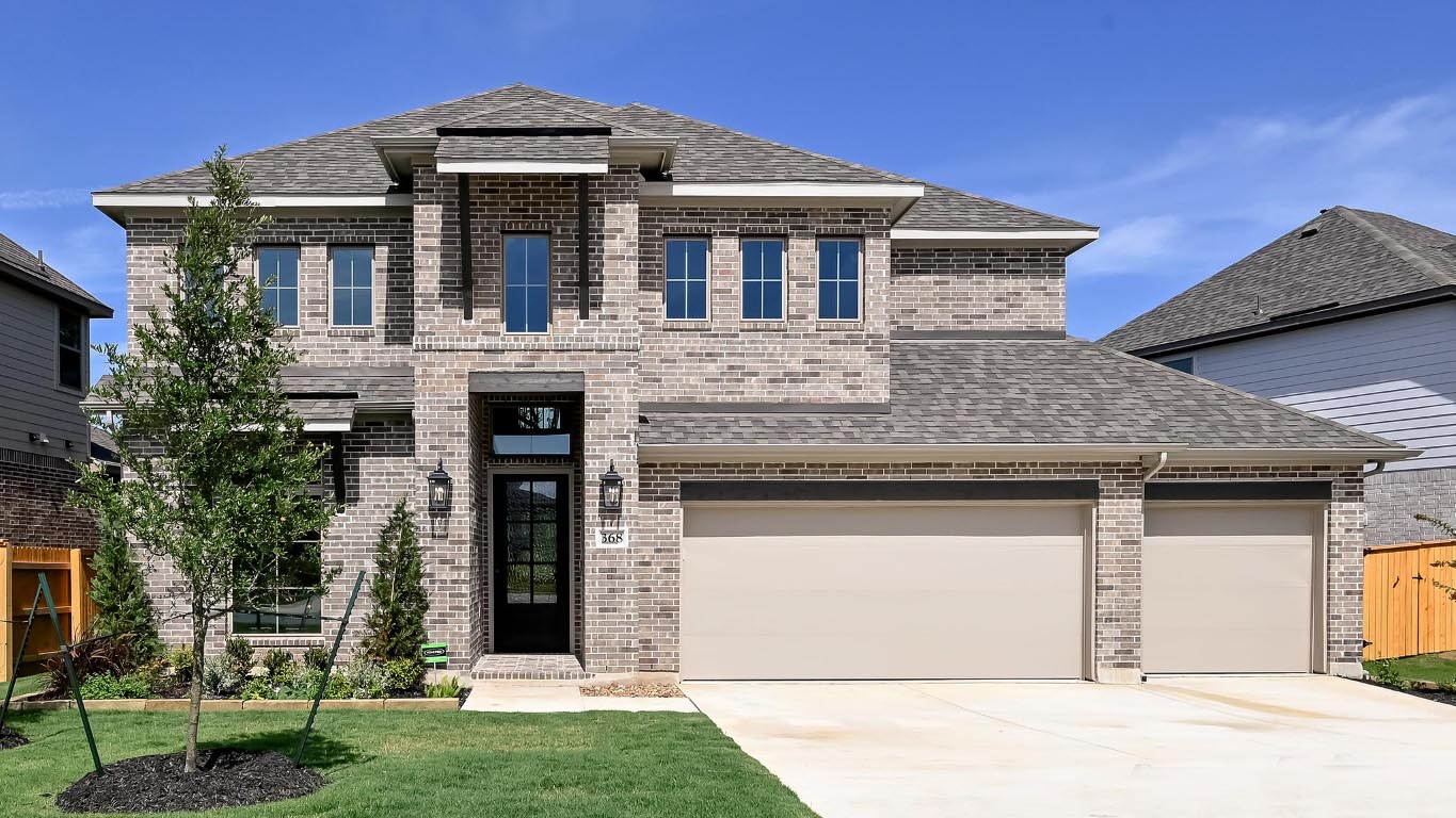 View of front of home with a shingled roof, driveway, brick siding, and an attached garage