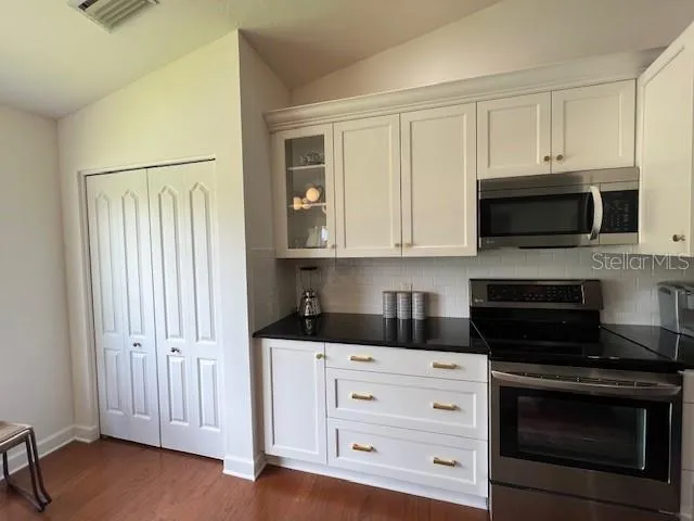 a kitchen with stainless steel appliances granite countertop white cabinets and black stove top oven with wooden floor