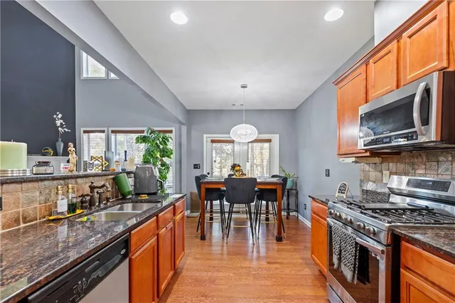 a kitchen with stainless steel appliances granite countertop a stove top oven a sink dishwasher a dining table and chairs with wooden floor