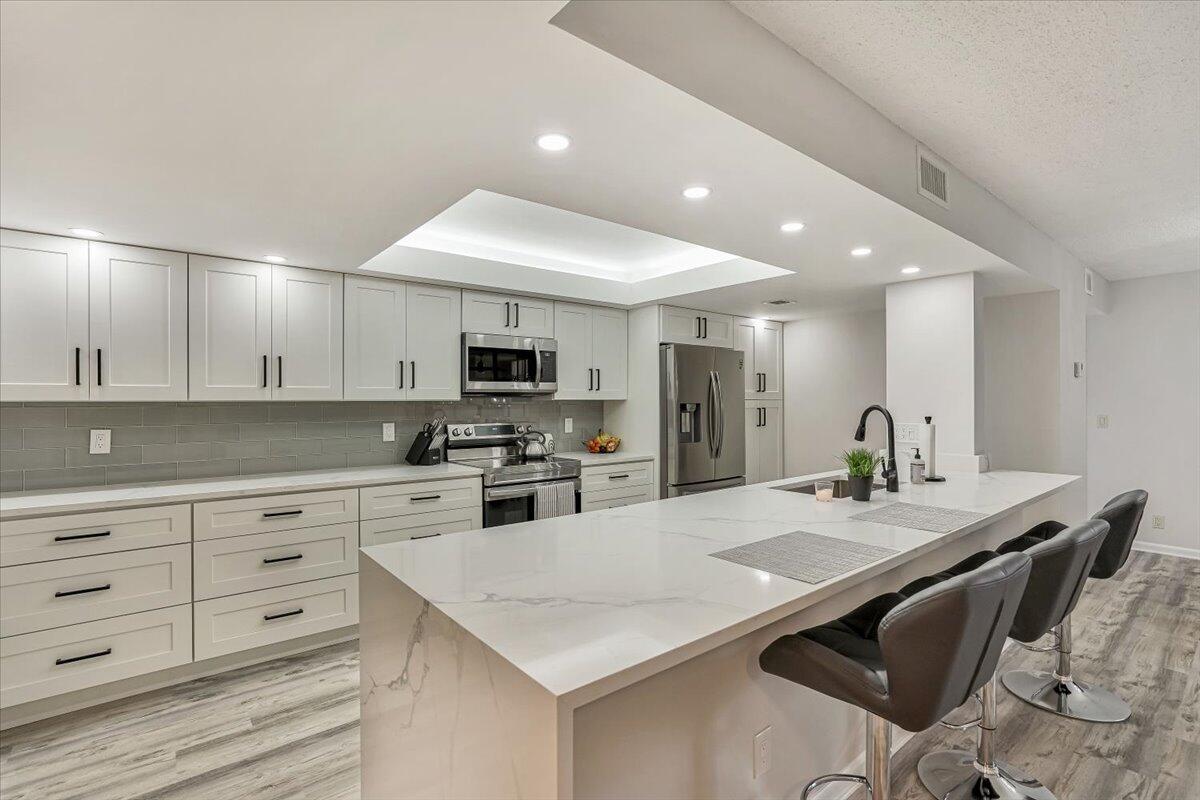 a kitchen with stainless steel appliances kitchen island granite countertop a stove a sink a refrigerator white cabinets and couches with wooden floor