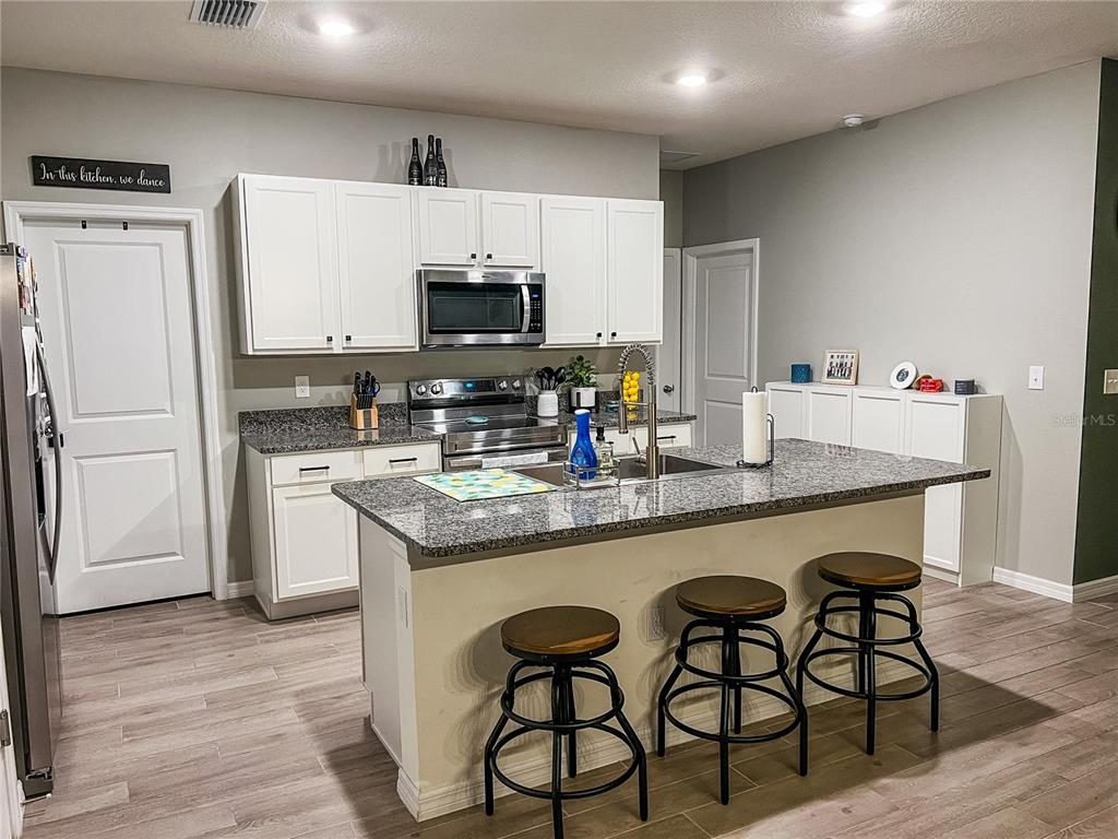 1439 Northwest 136th Street Gainesville, FL 32606 - Photo 6 of 28 a kitchen with stainless steel appliances granite countertop a stove a sink a microwave a refrigerator and white cabinets with wooden floor