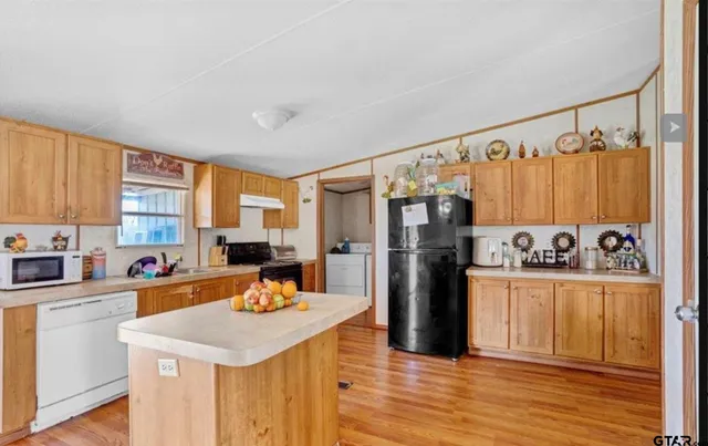 a kitchen with stainless steel appliances a stove a sink dishwasher a refrigerator white cabinets and wooden floor
