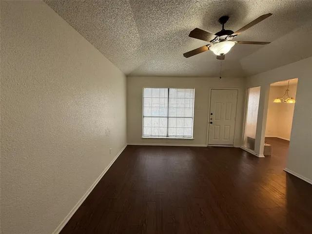 an empty room with wooden floor chandelier fan and windows