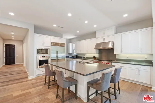 a kitchen with stainless steel appliances granite countertop a stove top oven a sink refrigerator and white cabinets with wooden floor