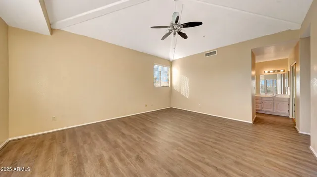 a view of an empty room with wooden floor and a ceiling fan