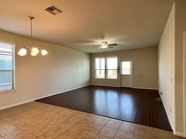a view of an empty room with window and chandelier fan