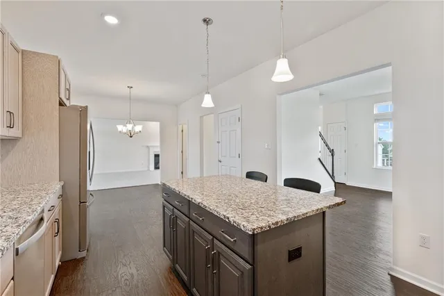 a kitchen with granite countertop kitchen island a refrigerator a sink dishwasher and wooden cabinets with wooden floor