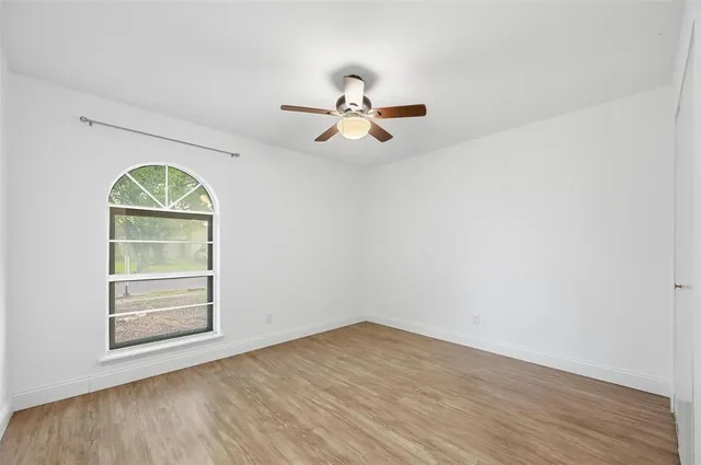 an empty room with wooden floor chandelier fan and windows