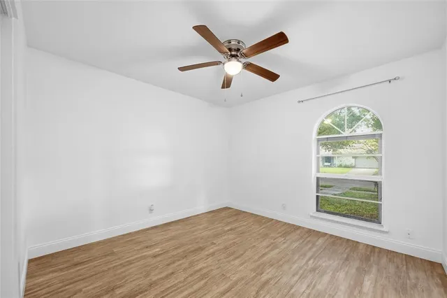an empty room with wooden floor a ceiling fan and window