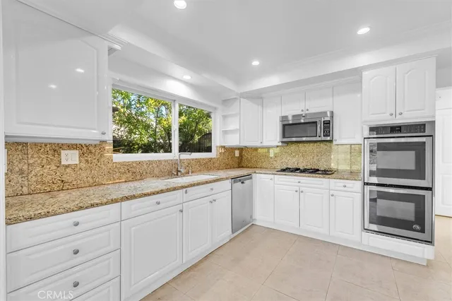 a kitchen with granite countertop white cabinets white stainless steel appliances with a sink and window