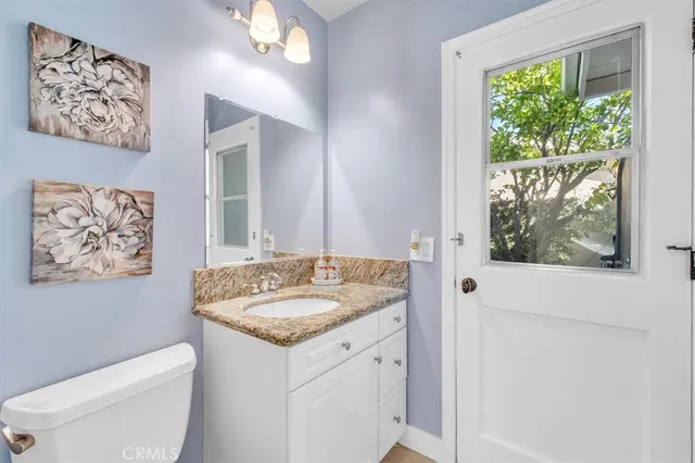 a bathroom with a granite countertop sink a toilet a large mirror and a window