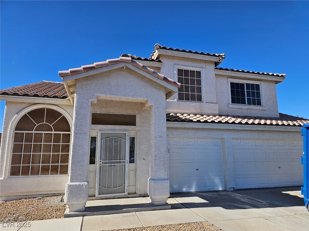 Mediterranean / spanish-style house featuring a tile roof, stucco siding, an attached garage, and driveway