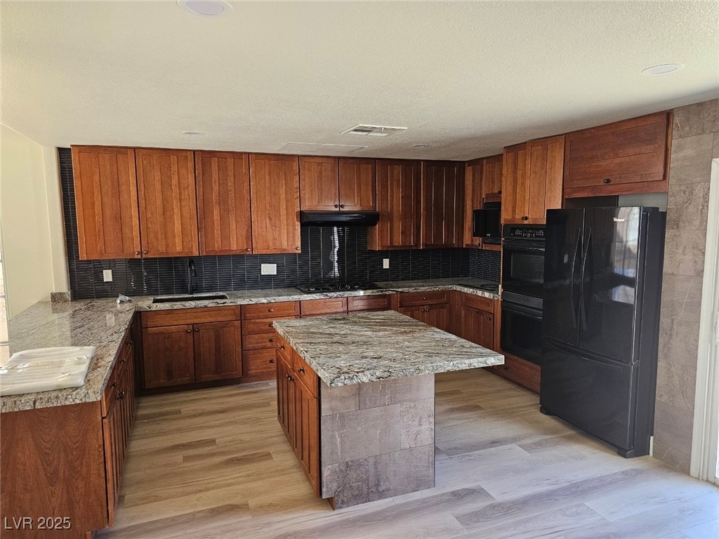 104 Appian Way Henderson, NV 89002 - Photo 45 of 52 Kitchen featuring black appliances, light stone counters, decorative backsplash, and a kitchen island