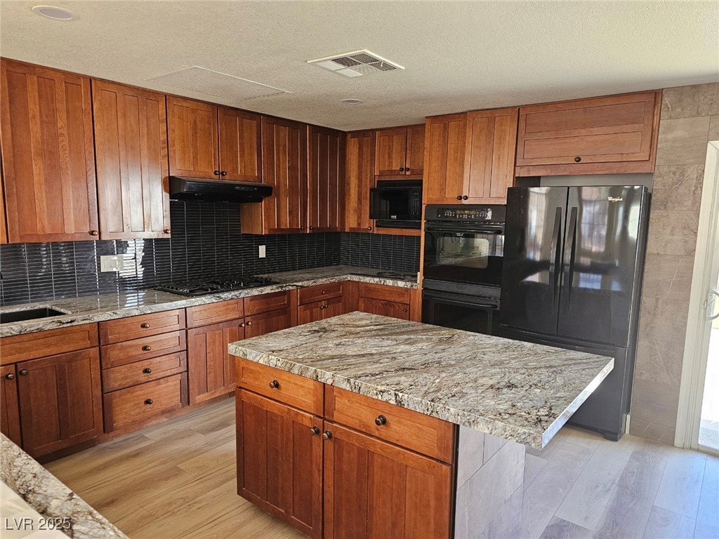 104 Appian Way Henderson, NV 89002 - Photo 46 of 52 Kitchen featuring black appliances, brown cabinets, light wood-style floors, tasteful backsplash, and a textured ceiling