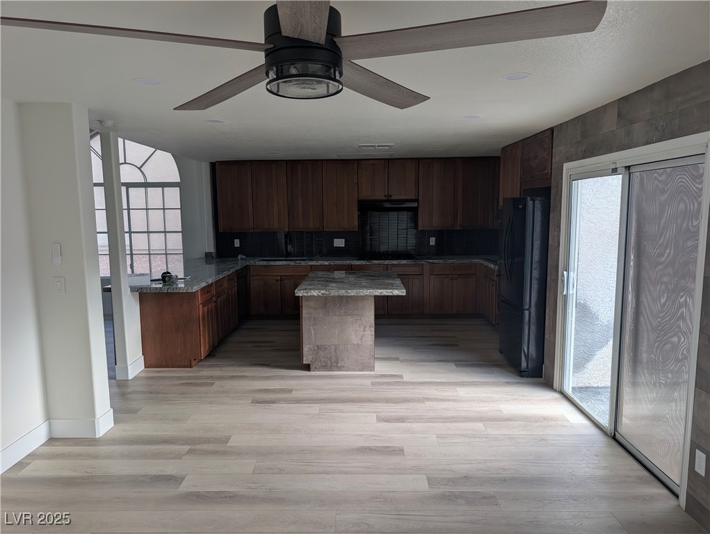 104 Appian Way Henderson, NV 89002 - Photo 4 of 52 Kitchen with a kitchen island, tasteful backsplash, black appliances, light wood-style flooring, and dark stone countertops