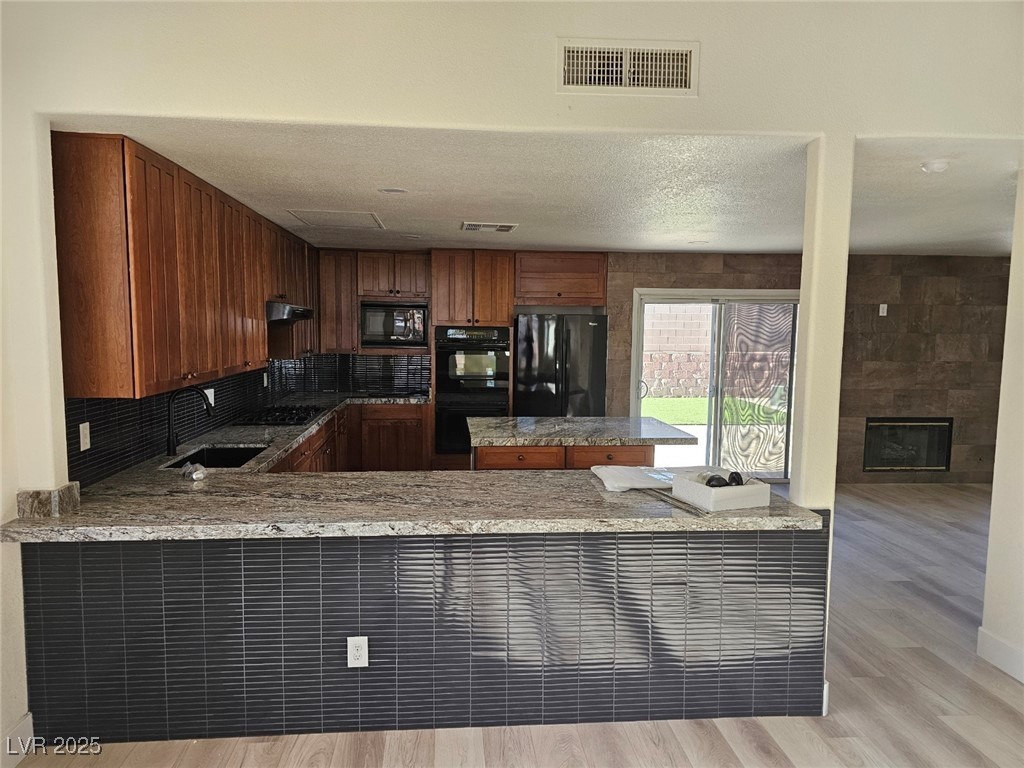 104 Appian Way Henderson, NV 89002 - Photo 51 of 52 Kitchen with black appliances, a peninsula, light wood-type flooring, light stone countertops, and a textured ceiling