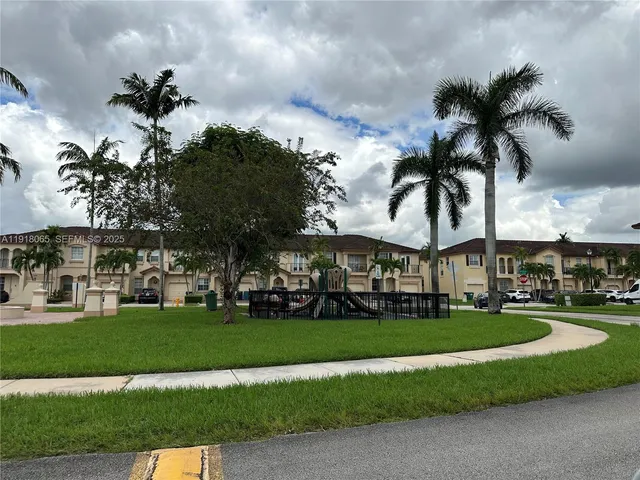 a view of a white house with a big yard and palm trees
