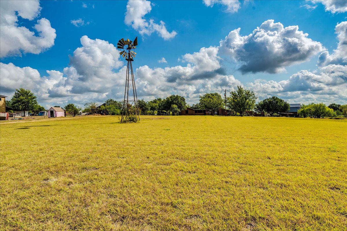 2411 Rohde Road Kyle, TX 78640 - Photo 10 of 40 A classic metal windmill stands tall over a wide grassy pasture under a blue sky.