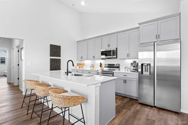 a kitchen with stainless steel appliances granite countertop a refrigerator a stove a sink and white cabinets with wooden floor