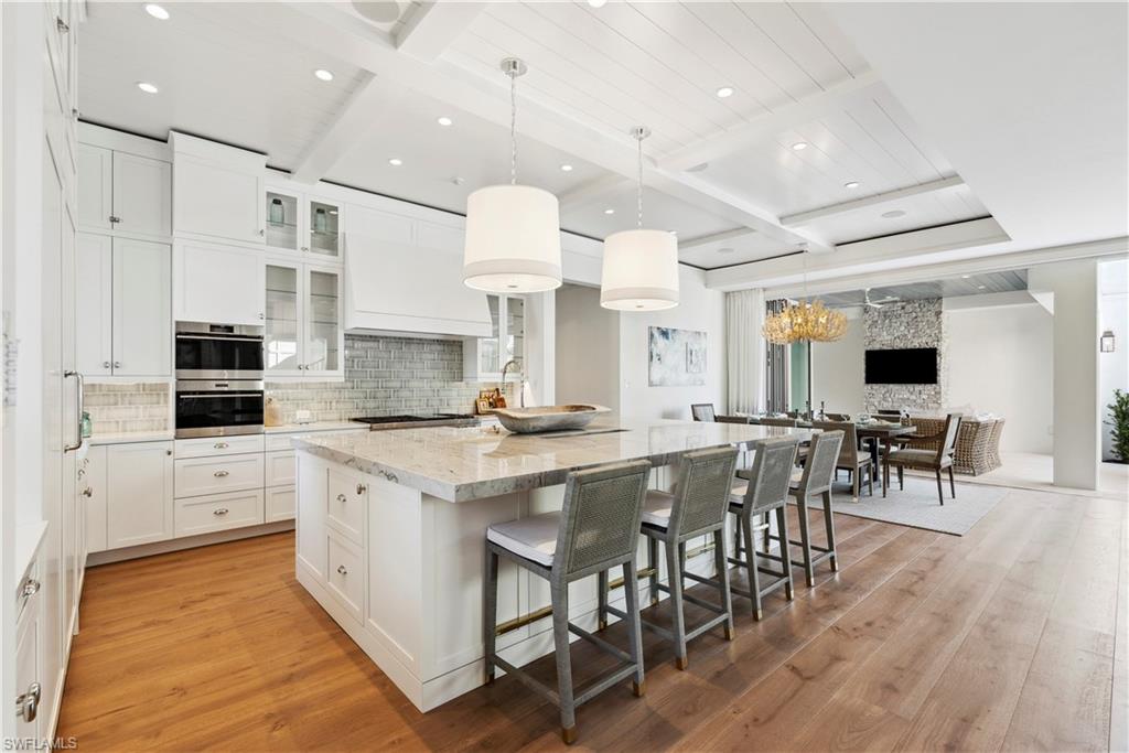 690 7th Avenue North Naples, FL 34102 - Photo 8 of 28 Kitchen with light stone countertops, decorative light fixtures, white cabinets, and a spacious island