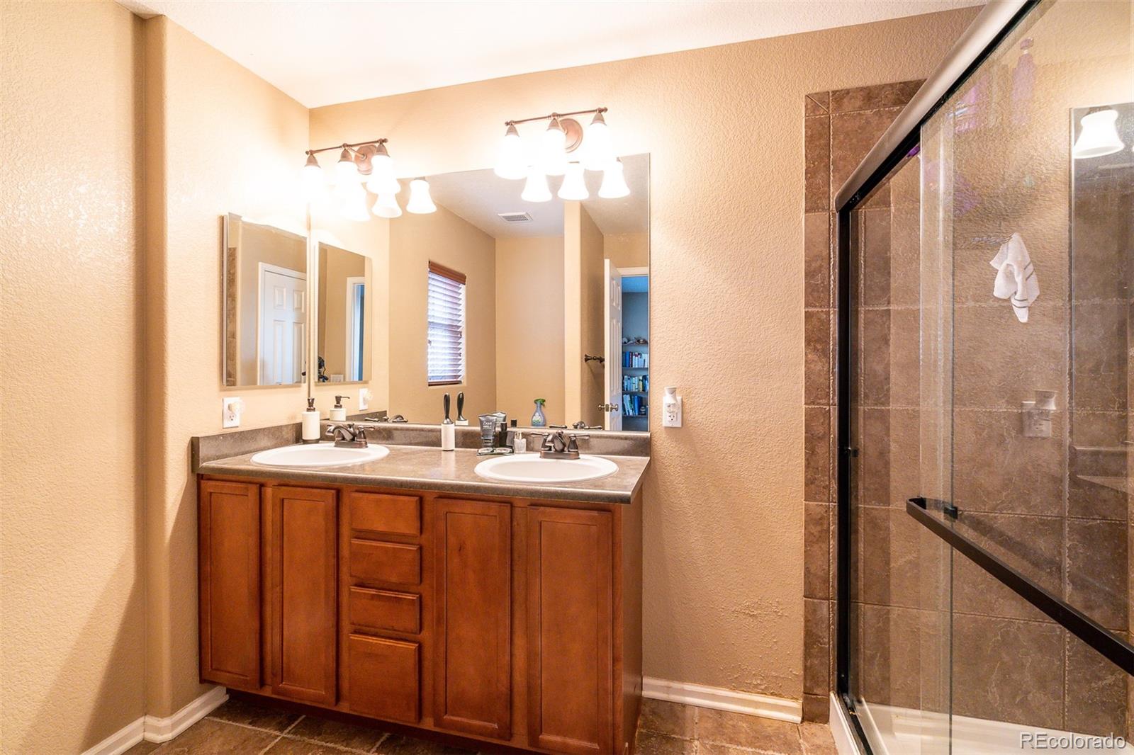 2681 Stonecrop Ridge Grove Colorado Springs, CO 80910 - Photo 18 of 26 a bathroom with a double vanity sink and mirror with shower