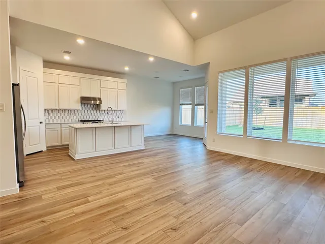a view of large kitchen with kitchen island wooden floor and stainless steel appliances