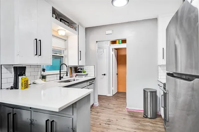 a kitchen with stainless steel appliances a refrigerator a sink a stove and white cabinets with wooden floor