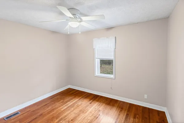 an empty room with wooden floor and fan