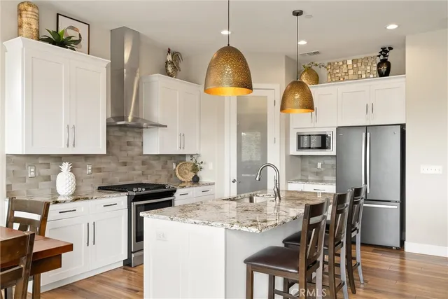 a kitchen with stainless steel appliances kitchen island granite countertop a stove a refrigerator a sink a dining table and chairs with wooden floor