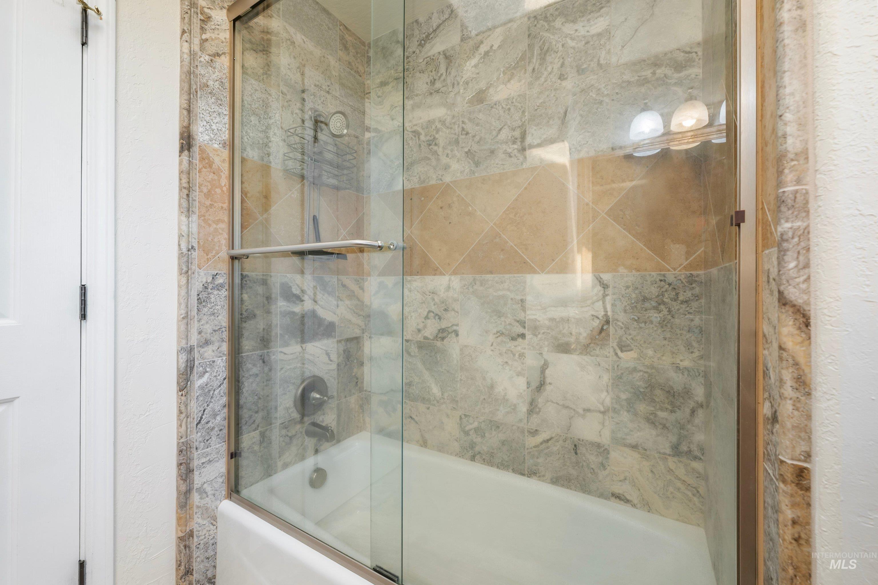 7657 Track Road Nampa, ID 83686 - Photo 31 of 50 Tub-shower combination with a sliding glass enclosure, multi-tone natural stone tile surround, and an integrated shelf