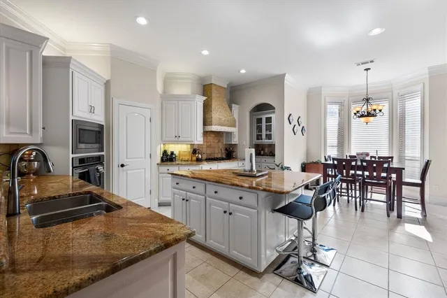 a kitchen with stainless steel appliances granite countertop a stove a sink a oven a dining table and chairs with white cabinets