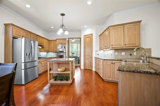 a kitchen with stainless steel appliances granite countertop a refrigerator a stove top oven a sink and dishwasher with wooden floor