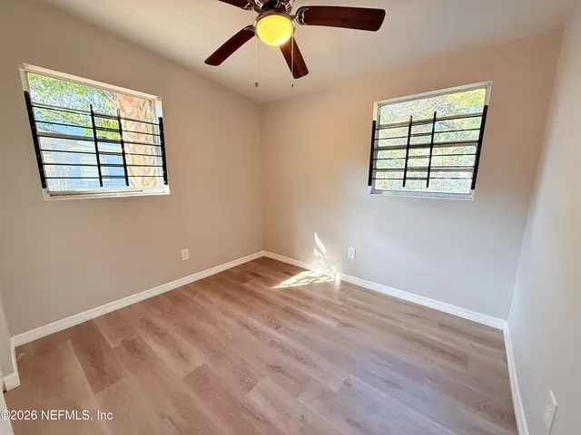 an empty room with wooden floor fan and windows