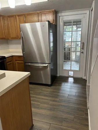 a view of a refrigerator in kitchen and an empty room with wooden floor