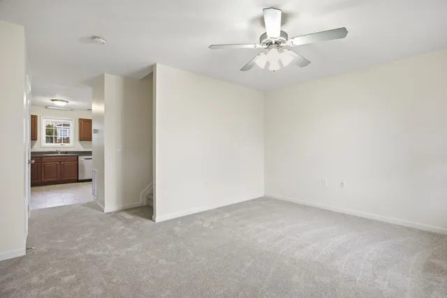 an empty room with chandelier fan and kitchen view
