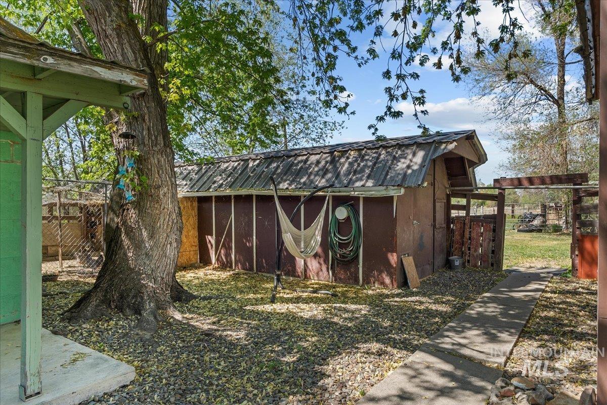 1958 East 1775 South Gooding, ID 83330 - Photo 42 of 49 Rear yard featuring a mature tree, a detached storage building with a corrugated metal roof, a concrete pathway, and a wood privacy fence