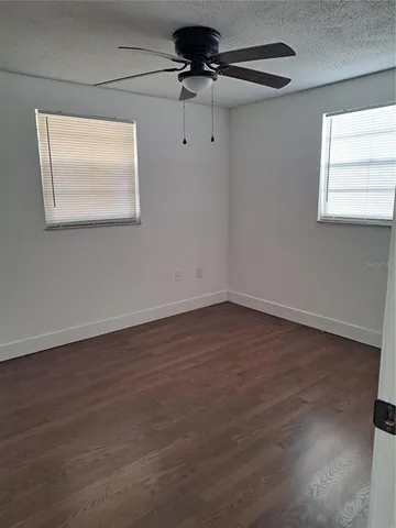 an empty room with wooden floor chandelier fan and windows
