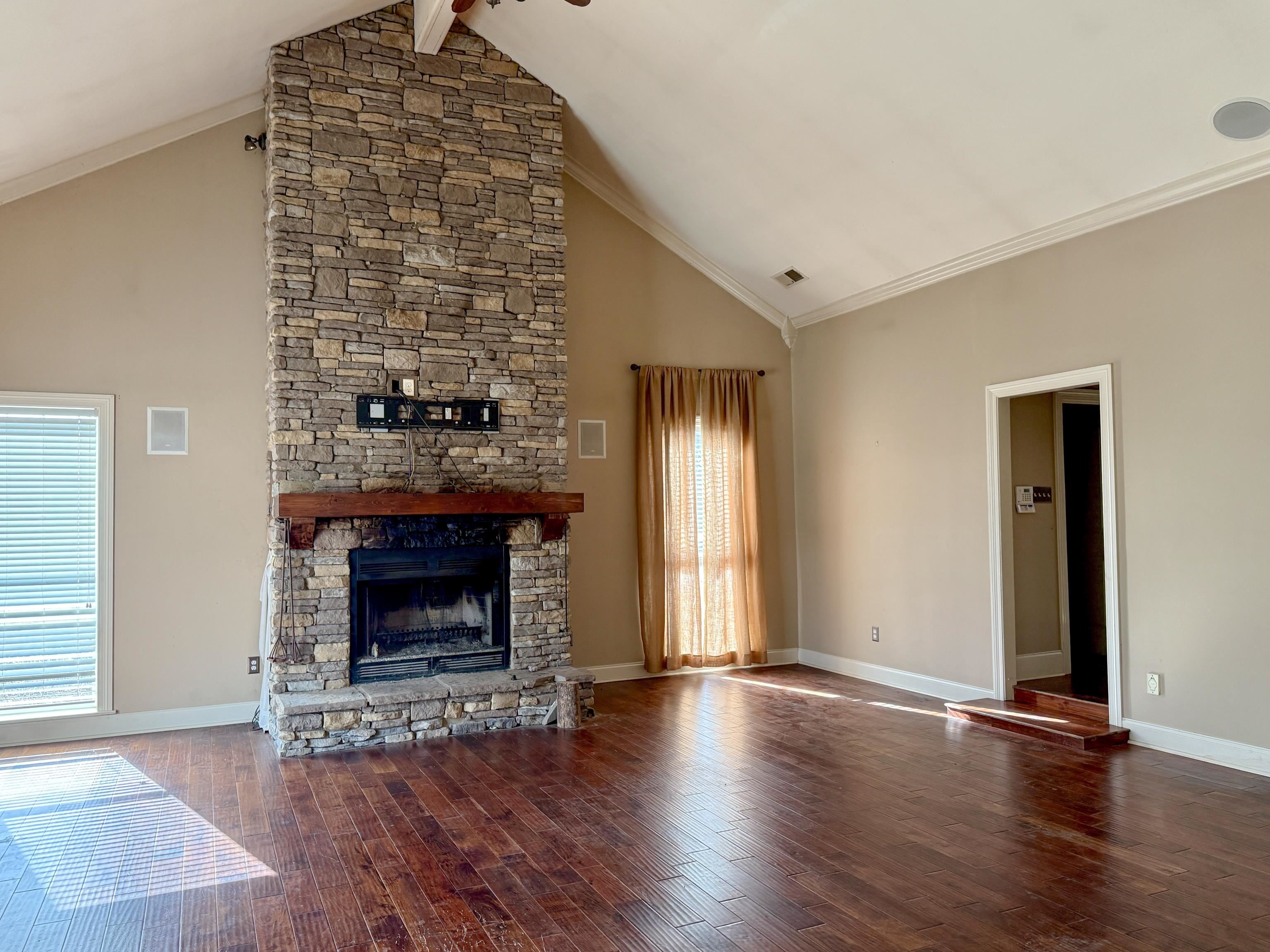 200 Diffee Road Moscow, TN 38057 - Photo 17 of 33 Unfurnished living room featuring high vaulted ceiling, a stone fireplace, wood-type flooring, and ornamental molding