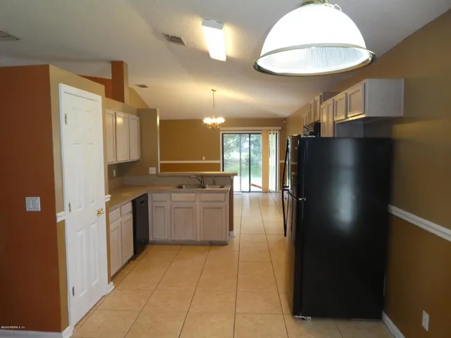 a view of a refrigerator in kitchen and an empty room in wooden floor