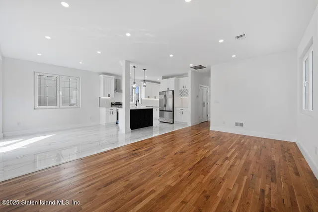 a view of empty room with wooden floor and kitchen