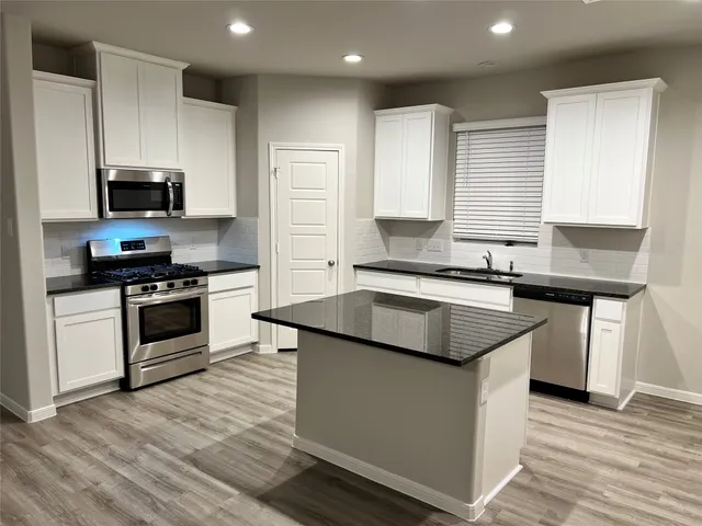 a kitchen with kitchen island granite countertop a sink cabinets and stainless steel appliances