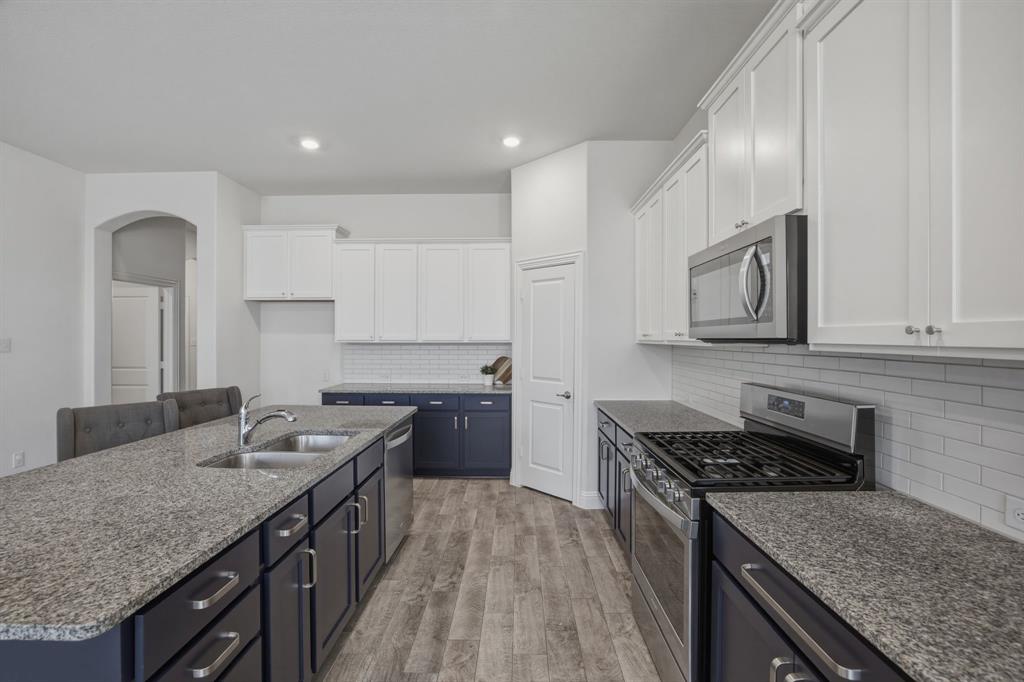 2909 Faro Road Aubrey, TX 76227 - Photo 8 of 32 a kitchen with granite countertop stainless steel appliances sink stove microwave and cabinets
