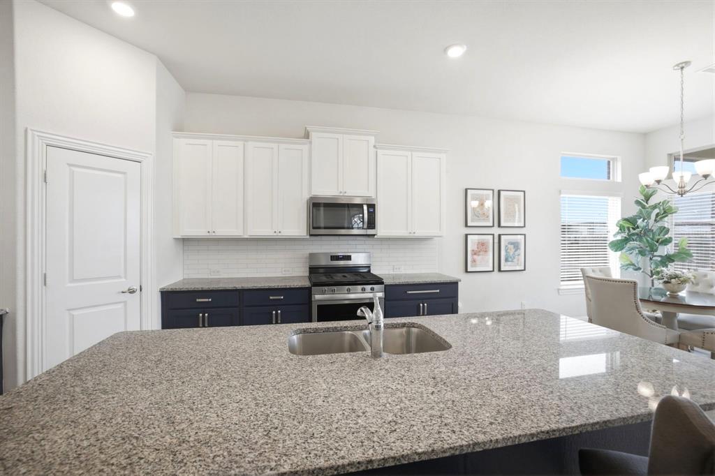 2909 Faro Road Aubrey, TX 76227 - Photo 10 of 32 a kitchen with granite countertop a stove top oven a sink a counter space and cabinets